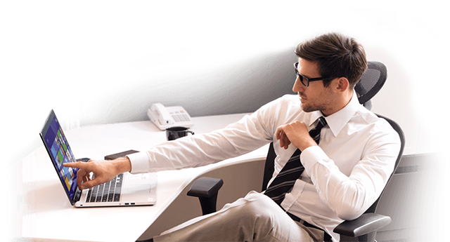 Man in a white shirt and black tie sitting in an office chair at a desk, 
				            pointing at a laptop screen.