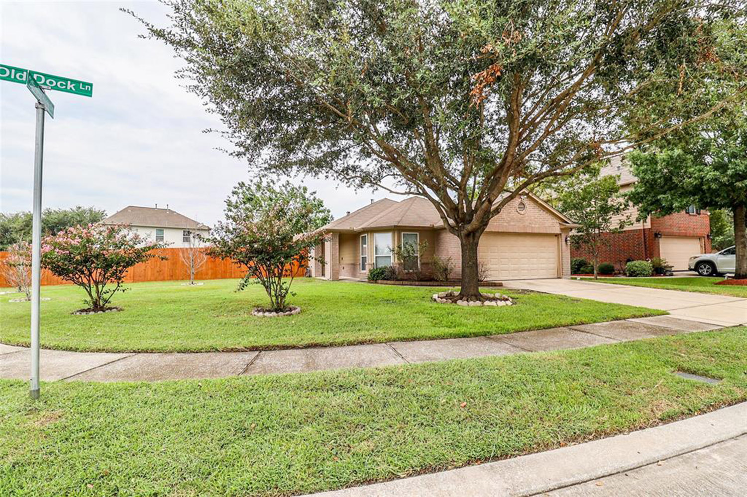 A single-story brick house with a landscaped yard, large tree, and a two-car garage, located on Old Dock Lane.